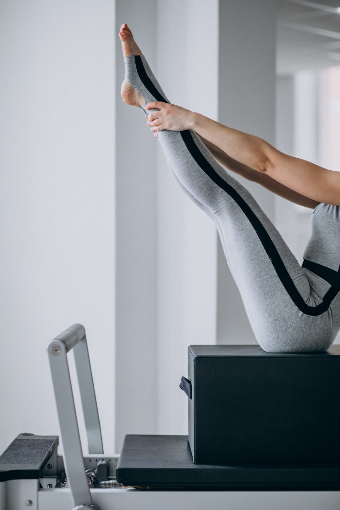 Máquina de Pilates reformer persona sobre cajón haciendo un ejercicio con las piernas extendidas
